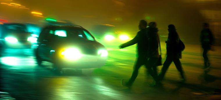 This image shows multiple people crossing a road at night as a car rapidly approaches.