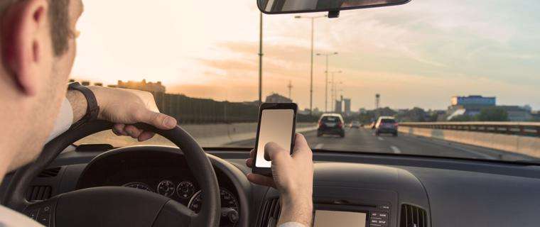 This image shows a man texting and driving. Atlanta pedestrian accident lawyers often see this causing injuries.