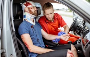 An injured passenger is receiving medical attention from a paramedic after a vehicle collision.