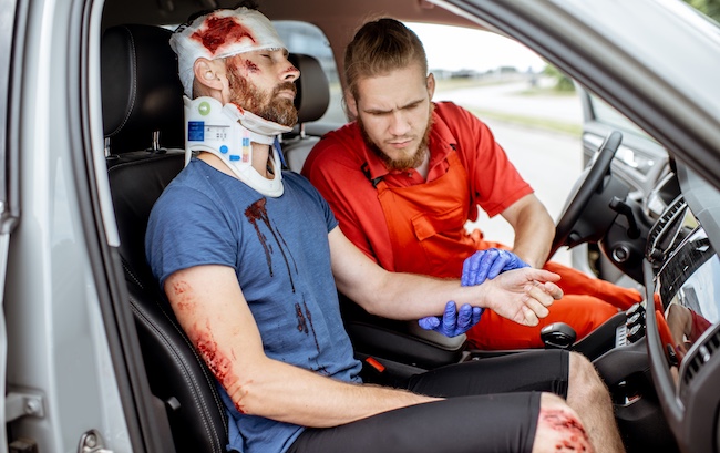 An injured passenger is receiving medical attention from a paramedic after a vehicle collision.