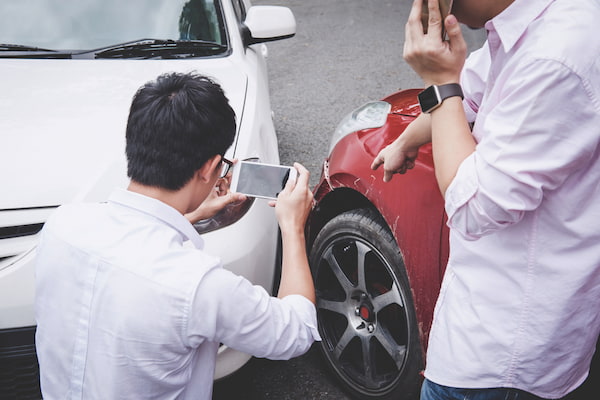 Two drivers argue while one takes photos after a car accident.